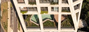 Profissional de sustentabilidade analisando projeto arquitetônico em edifício moderno com iluminação natural e vegetação interna.